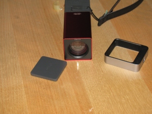 The Lytro camera. At left is the lens cover, it attaches magnetically. That's an item that will be lost immediately. Center, the camera, showing the front glass and lens. Right - a tripod adaptor.